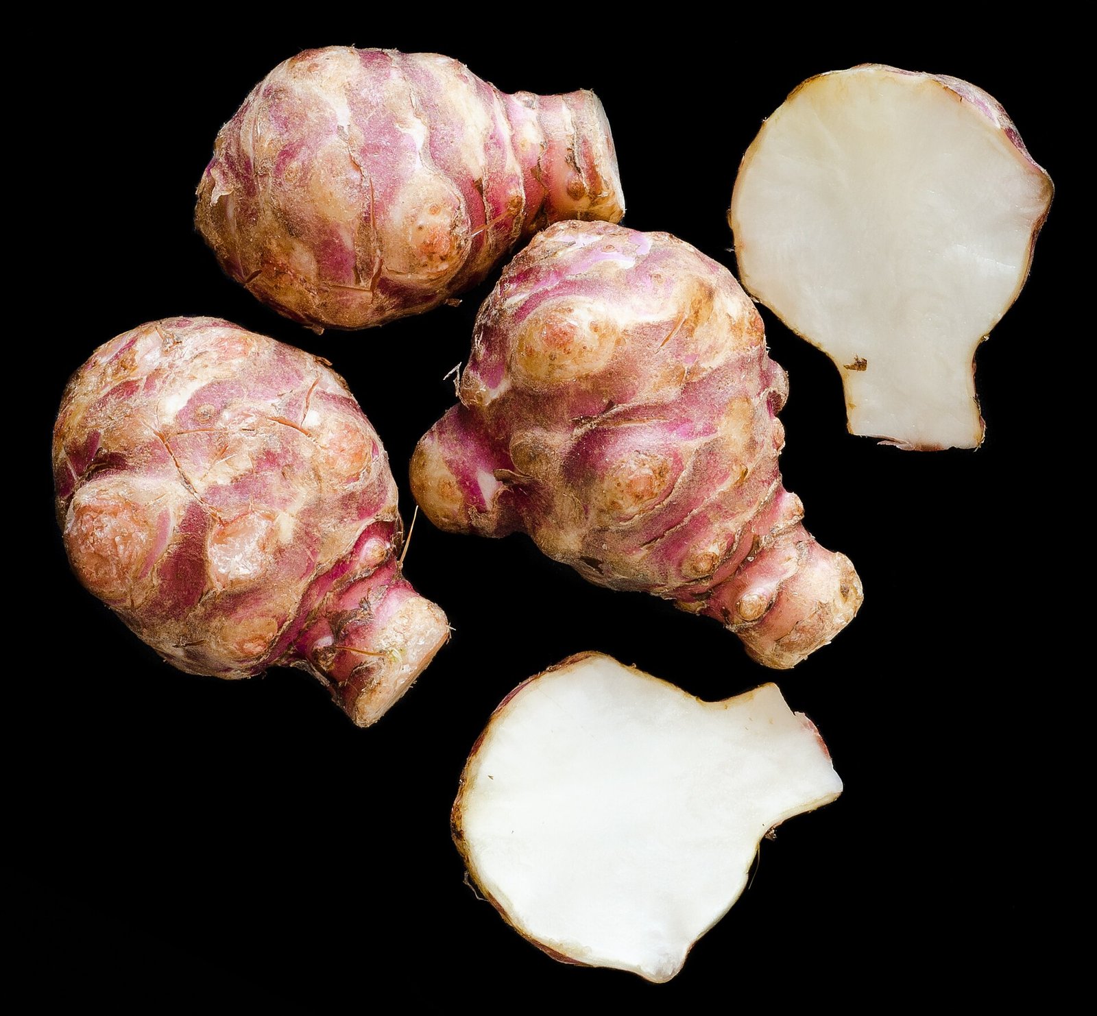 Tubercules de topinambour entiers et coupés sur fond noir